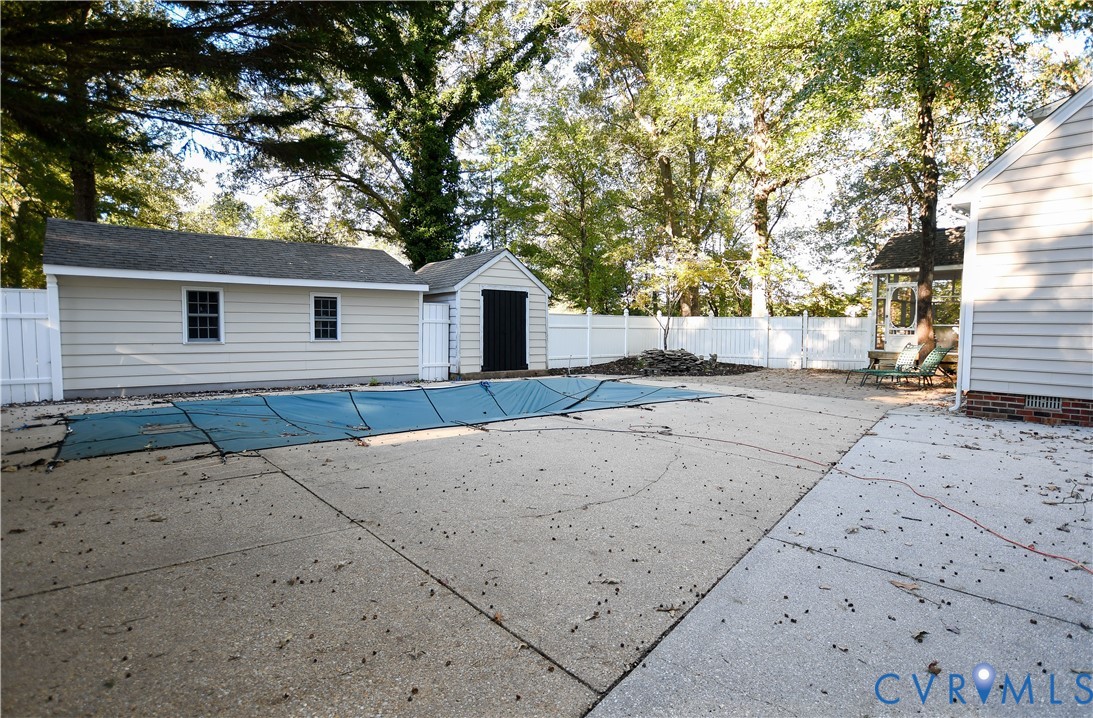 Backyard featuring a concrete pool deck, fenced perimeter, detached storage structure, and siding exterior