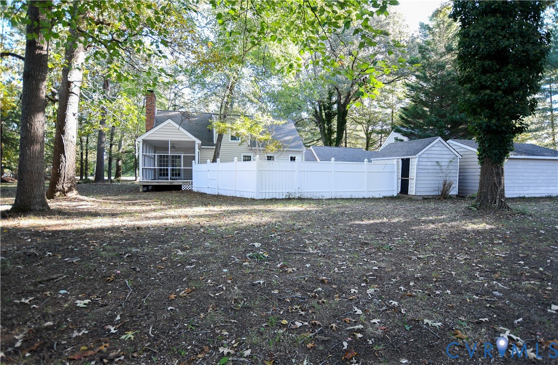 Large private backyard featuring mature trees, white vinyl privacy fencing, a screened porch, and detached storage structures