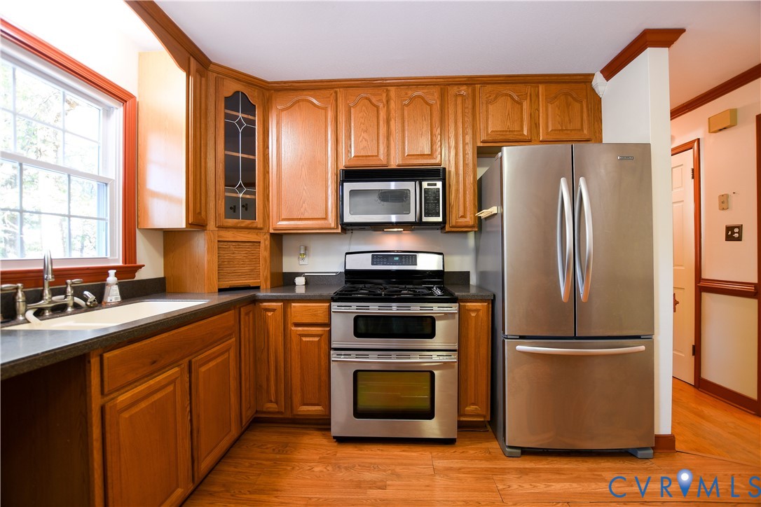 Kitchen featuring oak cabinetry with integrated glass-paneled display shelving, stainless steel appliances, a double-oven range, and wood-finish flooring