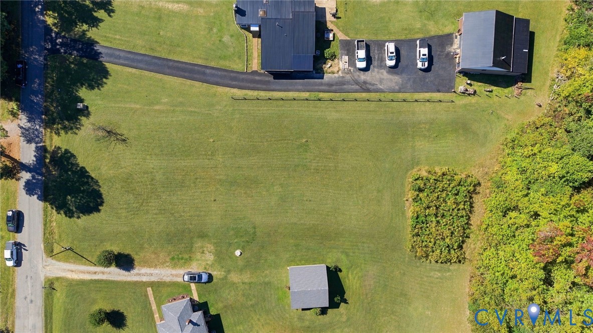 Expansive acreage featuring a manicured lawn, paved driveway, detached structure, and mature tree borders