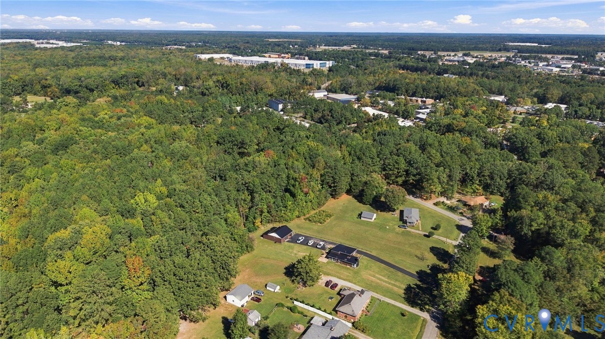 Aerial perspective featuring expansive forested acreage, multiple cleared grass parcels, and paved driveway access