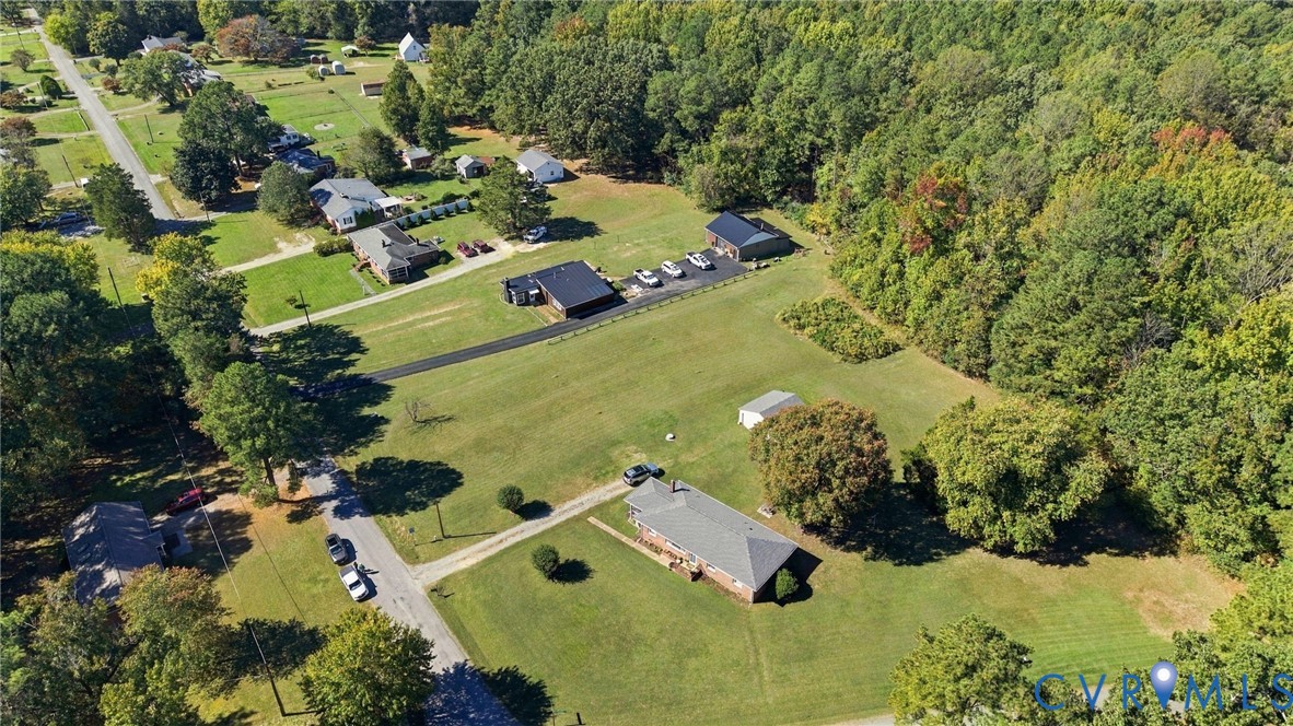 Aerial perspective of a sprawling lot featuring a single-story residence, a detached multi-bay garage, expansive lawn areas, and mature tree borders