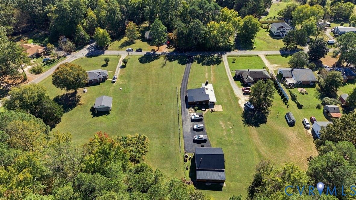 Aerial view featuring expansive acreage, a paved private driveway, a standalone multi-level structure, and mature perimeter trees