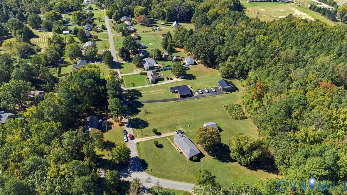Aerial perspective of a multi-structure parcel featuring expansive open green space, mature tree cover, a paved driveway, and detached storage outbuildings