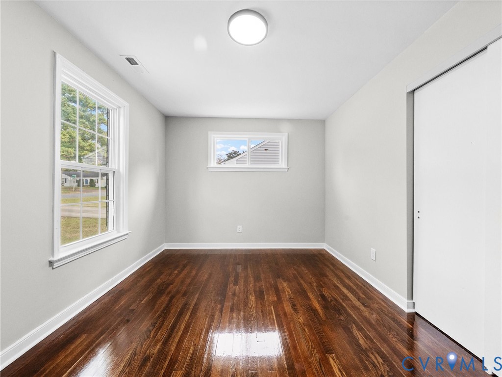 Room featuring polished wood-finish flooring, neutral wall paint, a double-hung window, a slider window, and a built-in closet with sliding doors