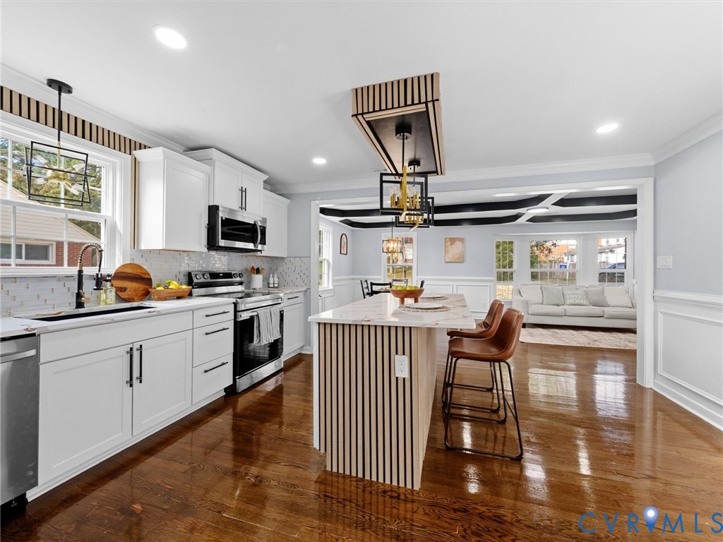 Kitchen featuring white cabinetry, wood-finish flooring, a kitchen island with vertical wood-slat detailing, stone-finish countertops, and geometric pendant lighting