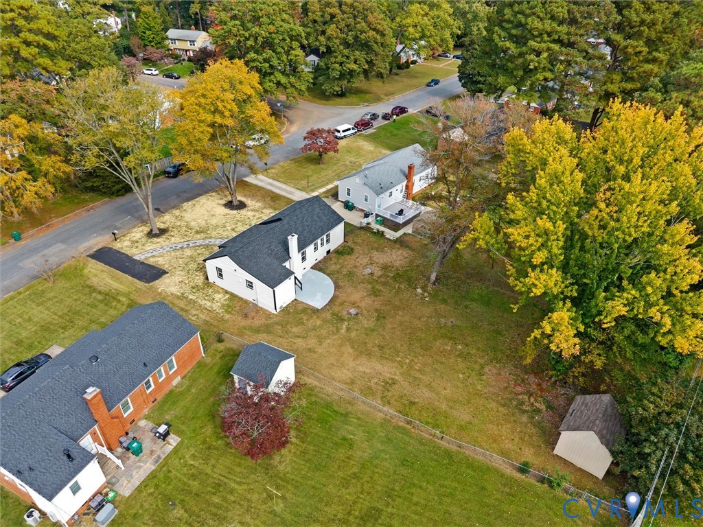 Aerial perspective of a property featuring a sprawling lot, mature trees, a detached storage structure, a stone-paved walkway, and a rear circular patio