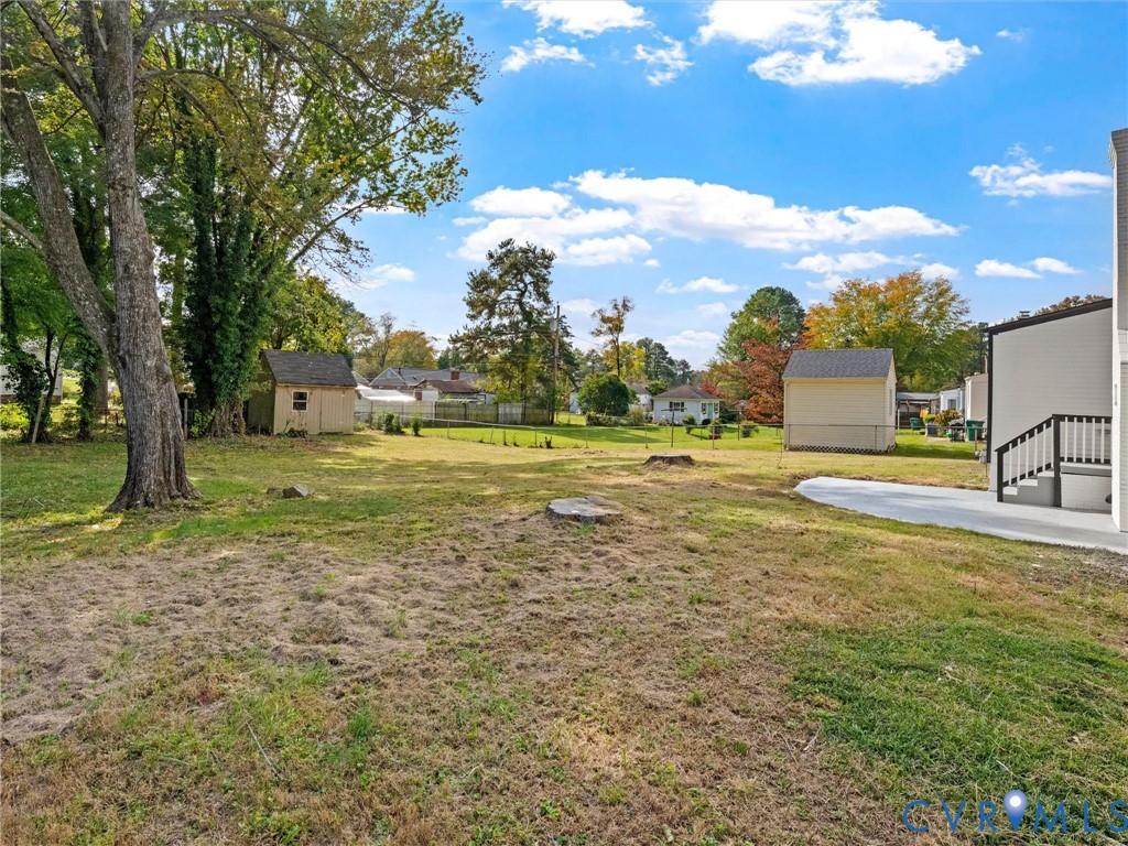 Expansive backyard featuring a concrete patio, detached storage structures, and mature trees