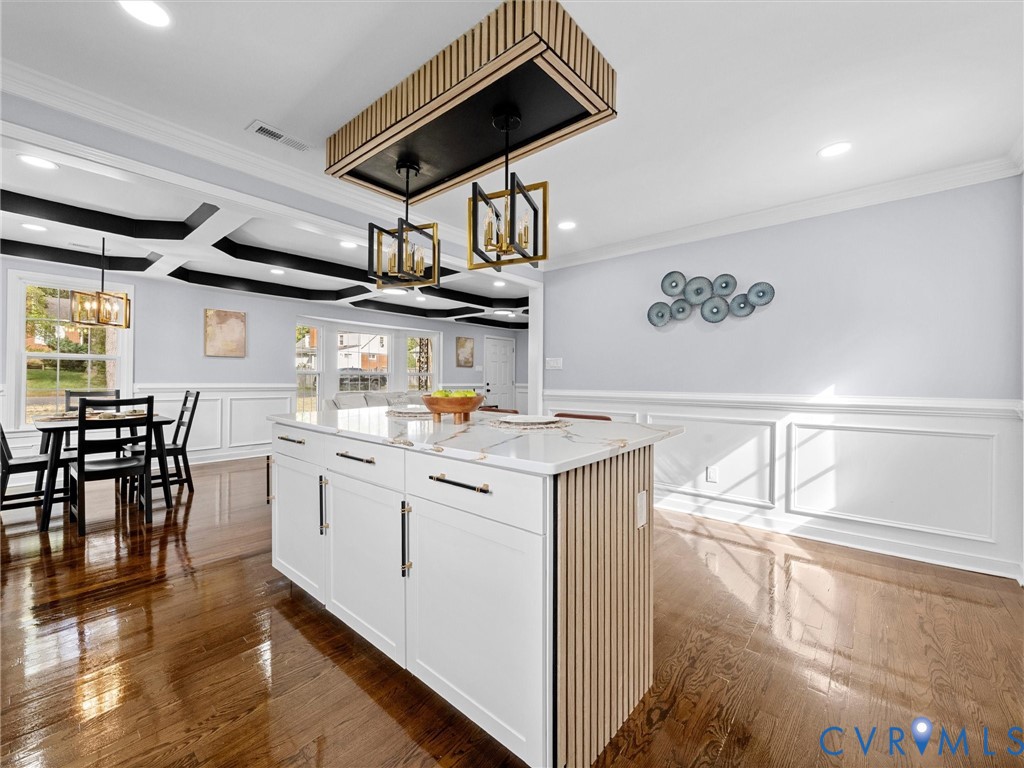Kitchen island featuring white cabinetry with vertical wood-slat detailing, stone countertop, coffered ceiling with black accents, and pendant light fixtures