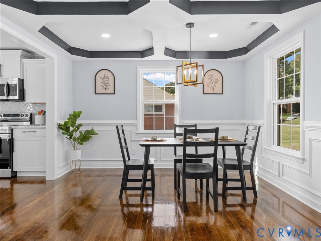 Dining area featuring a coffered ceiling with dark trim, wainscoting, wood-finish flooring, and a multi-light geometric pendant fixture