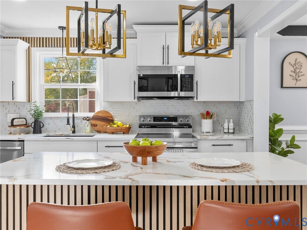 Kitchen featuring white shaker-style cabinetry, a central island with a wood-slat base and quartz countertop, stainless steel appliances, and dual geometric-frame pendant light fixtures