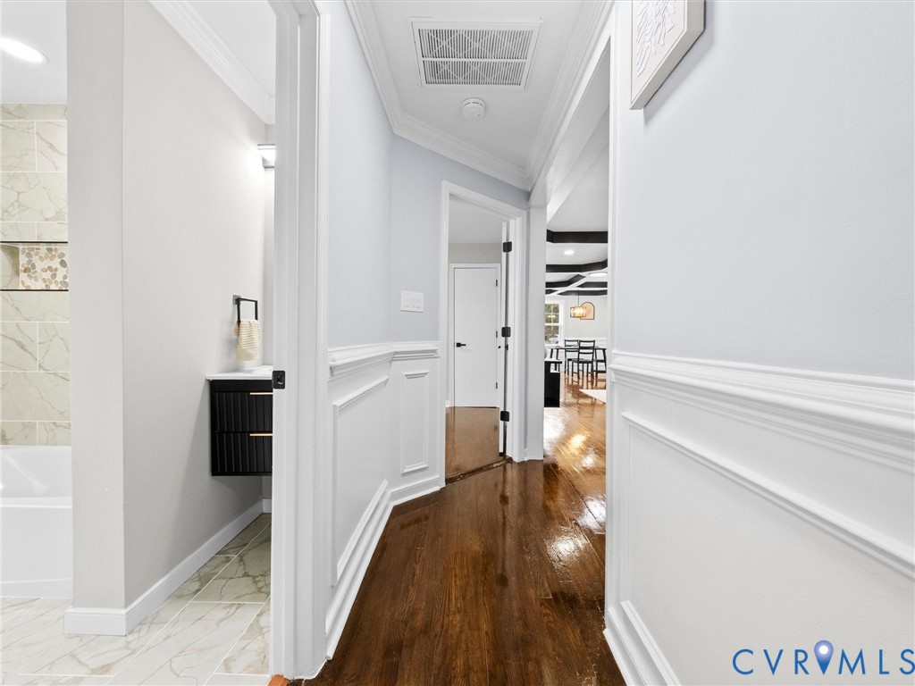 Hallway featuring crown molding, wainscoting, and wood-finish flooring, complemented by a black floating vanity and tiled tub surround