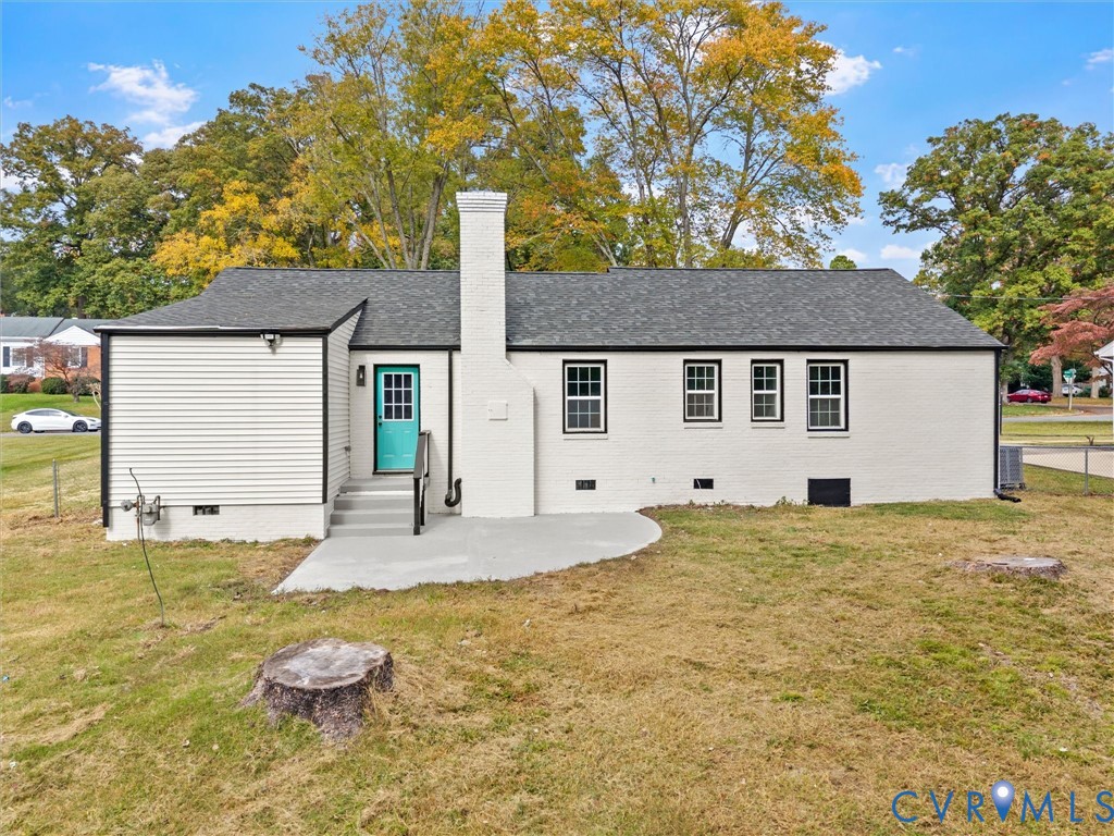 Painted brick and siding exterior featuring a centered masonry chimney, rear concrete patio, and grid-pattern window panes