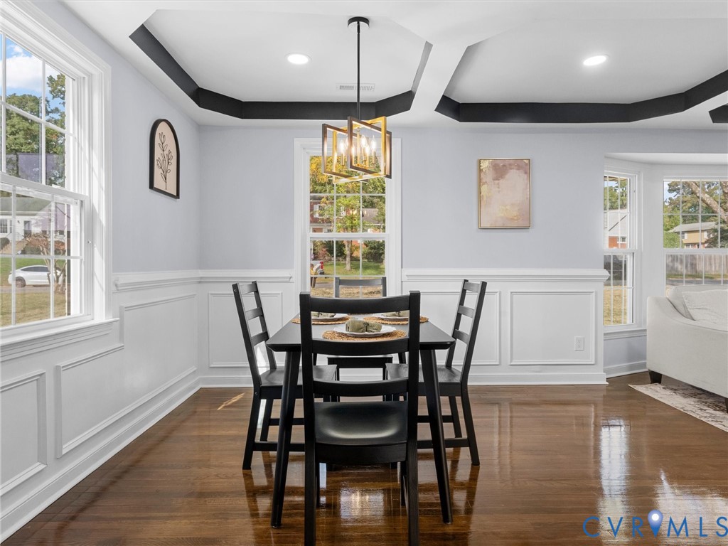 Dining area featuring a tray ceiling with high-contrast crown molding, polished wood-finish flooring, wainscoting, and a geometric metal chandelier