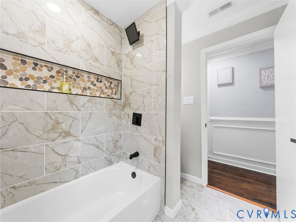 Shower enclosure with large-format tile walls, recessed pebble-stone accent niche, matte black fixtures, and built-in tub
