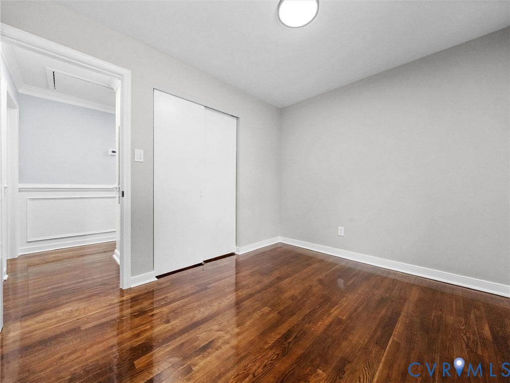 Interior room featuring polished wood-finish flooring, neutral wall paint, a double-panel closet door, and a flush-mount ceiling light fixture