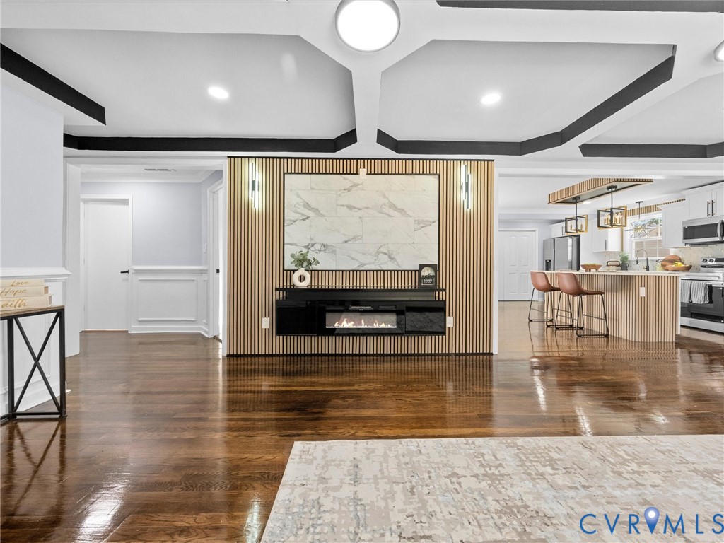 Coffered ceiling with contrasting trim, wood-slat accent wall, wall-mounted electric fireplace, stone-finish fireplace surround, and wood-finish flooring