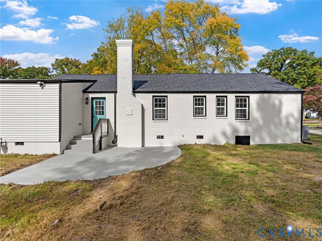 Exterior featuring painted brick siding, a prominent central masonry chimney, concrete patio, and a shingled roof
