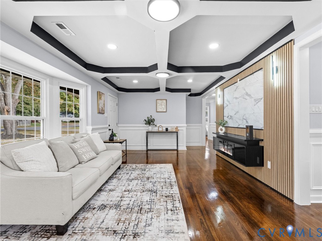 Coffered ceiling with dark accent trim, wood-finish flooring, and a floor-to-ceiling slatted wood accent wall featuring a stone-patterned panel and a mounted electric fireplace