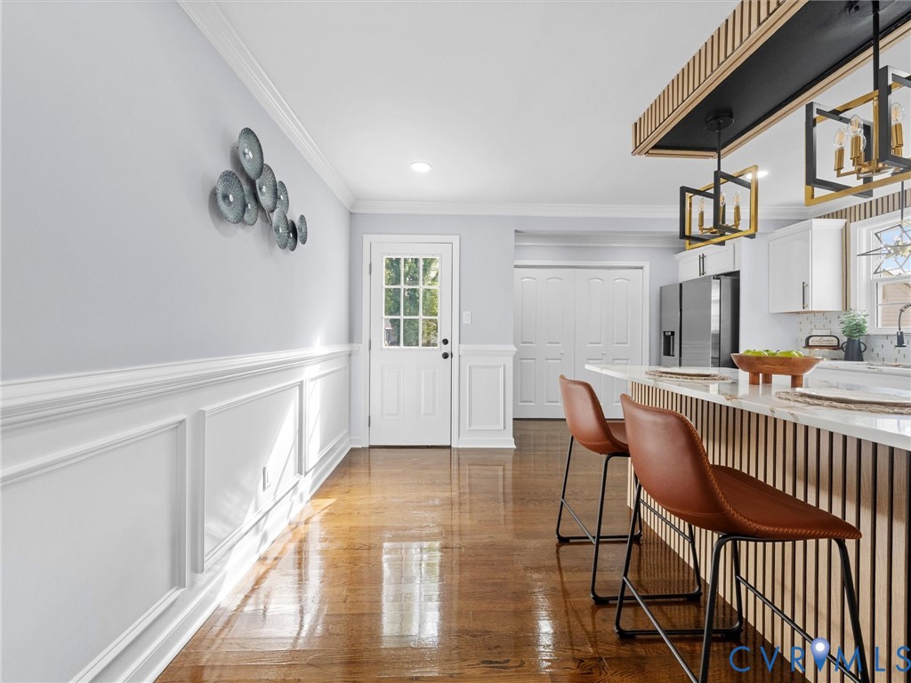 Wood-finish flooring, wainscoting, a kitchen island with vertical wood-slat detailing, stone-finish countertops, and geometric pendant lighting