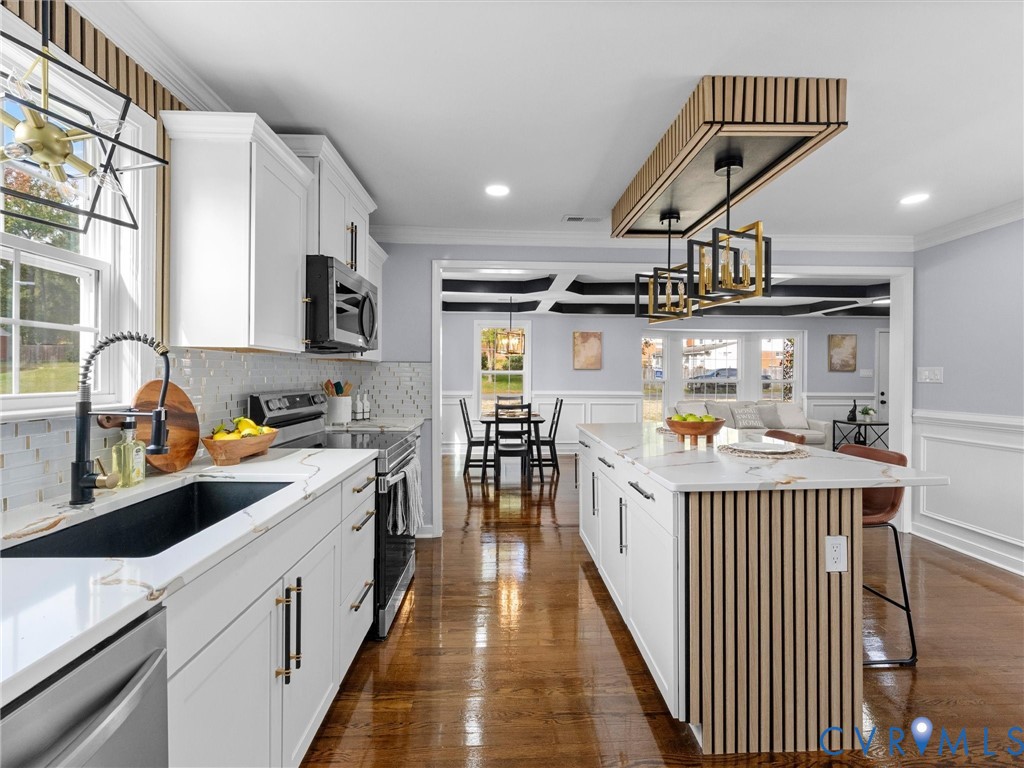 Kitchen featuring a center island with slatted wood detailing, white cabinetry, stone-finish countertops, geometric pendant lighting, and wood-finish flooring