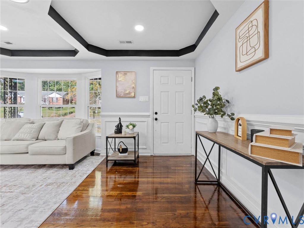 Tray ceiling with dark accent molding, bay window, wood-finish flooring, and white wainscoting Tray ceiling with dark accent molding, bay window, wood-finish flooring, and white wainscoting
