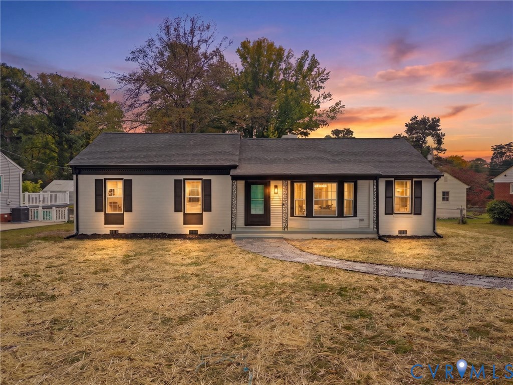 Single-story exterior featuring a light-toned painted brick facade, dark-finish shutters, a prominent bay window, and a covered front porch entry Single-story exterior featuring a light-toned painted brick facade, dark-finish shutters, a prominent bay window, and a covered front porch entry