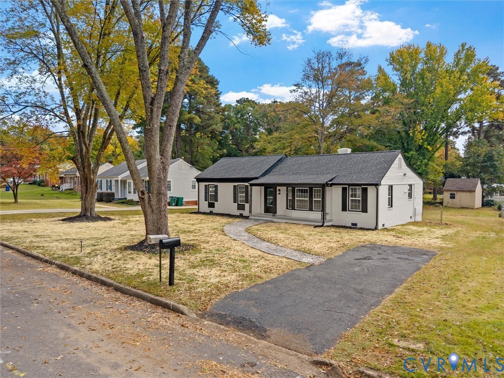 Single-story exterior featuring painted brick siding, black shutter accents, a shingled roof, a paved walkway, and a detached storage structure Single-story exterior featuring painted brick siding, black shutter accents, a shingled roof, a paved walkway, and a detached storage structure