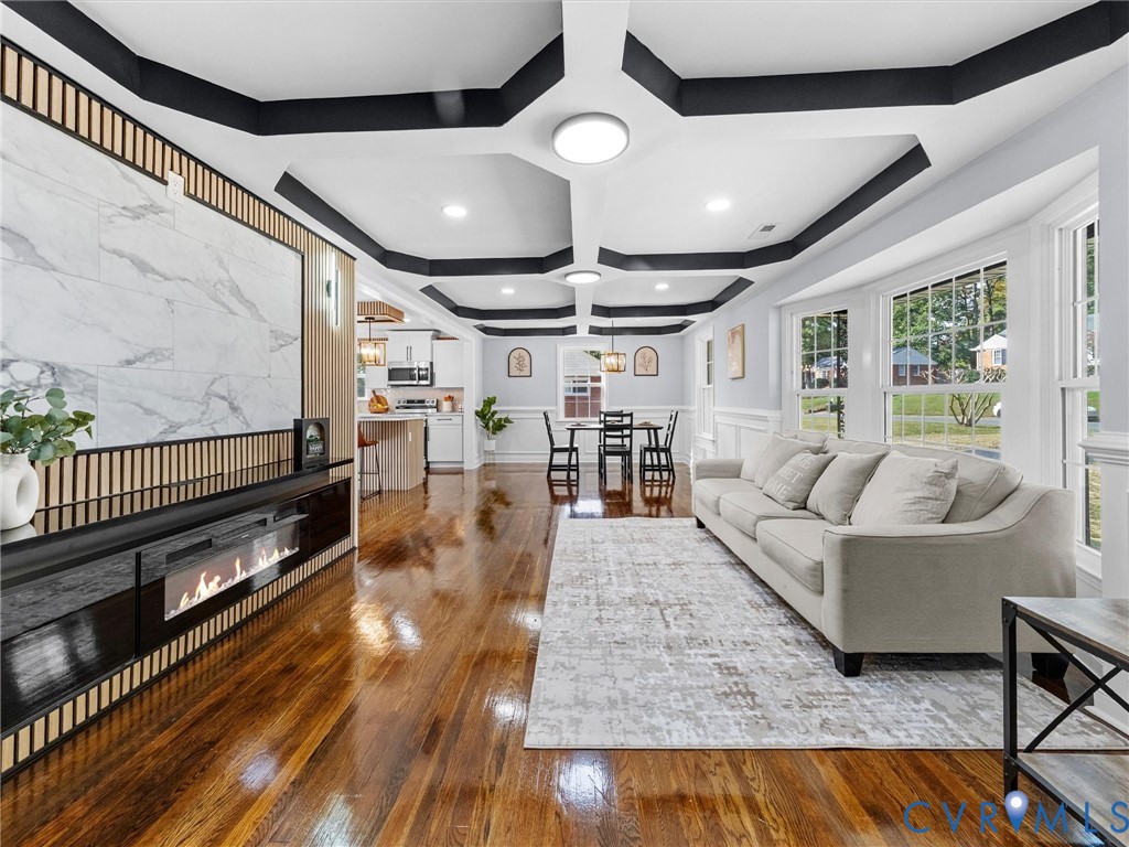 Coffered ceiling with contrasting trim, stone-finish accent wall, built-in horizontal fireplace, wood-finish flooring, and crown molding