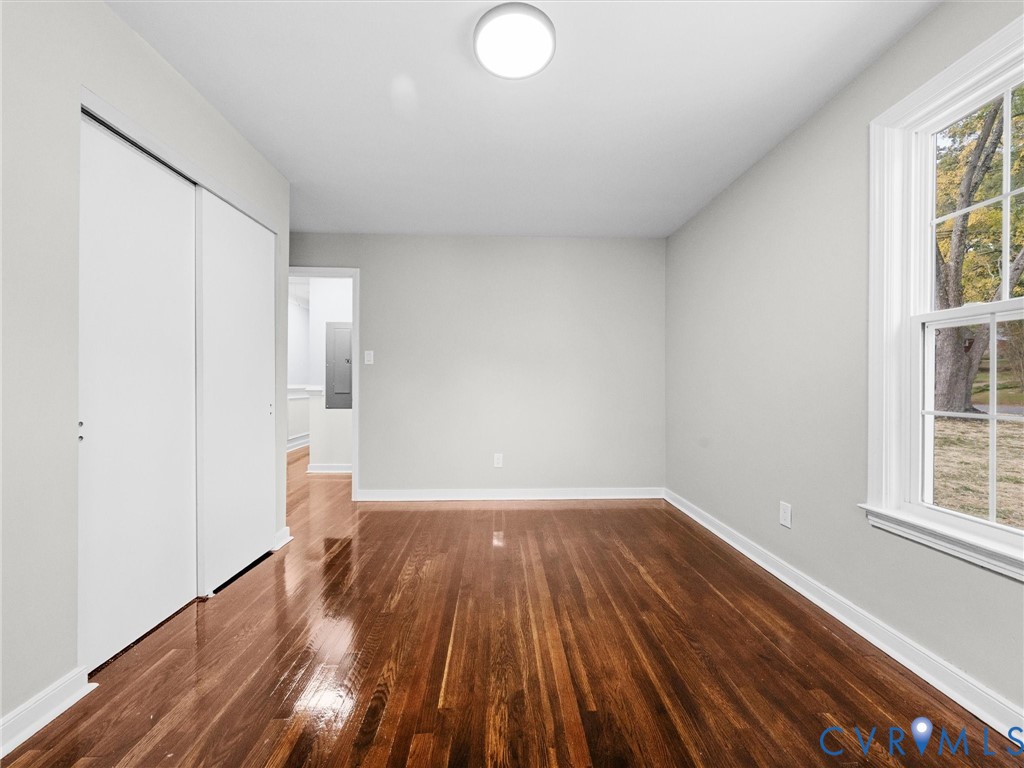 Polished wood-finish flooring, dual-panel sliding closet doors, neutral wall palette, and double-hung window with exterior landscape exposure