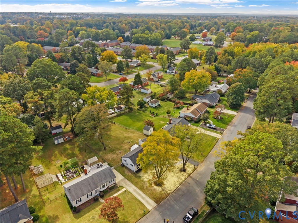 Aerial perspective showcasing a residential property with a detached storage structure, concrete driveway, and established landscape featuring mature trees on a level lot