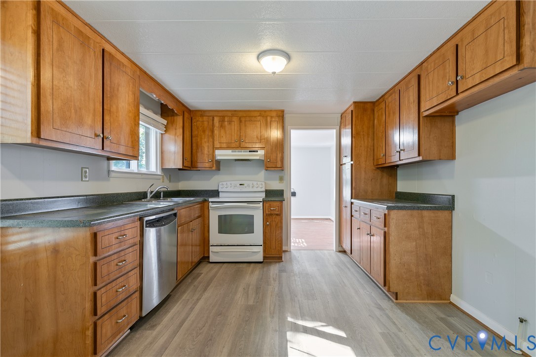 Kitchen featuring wood cabinetry, solid surface countertops, wood-finish flooring, a stainless steel dishwasher, and a white range
