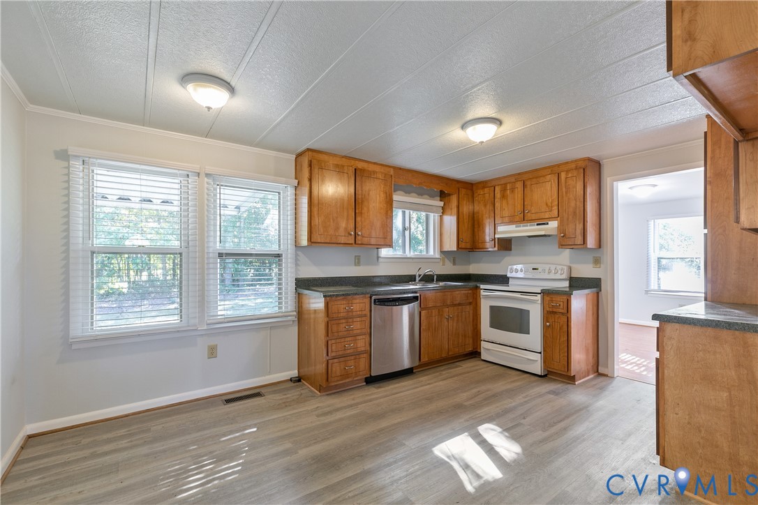 Kitchen featuring wood-finish cabinetry, dark solid-surface countertops, stainless steel dishwasher, white range, and wood-finish flooring