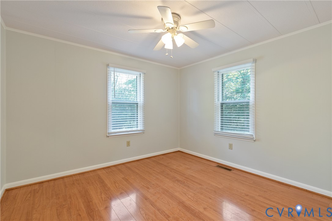 Room featuring wood-finish flooring, two windows with horizontal blinds, and a central ceiling fan with integrated lighting
