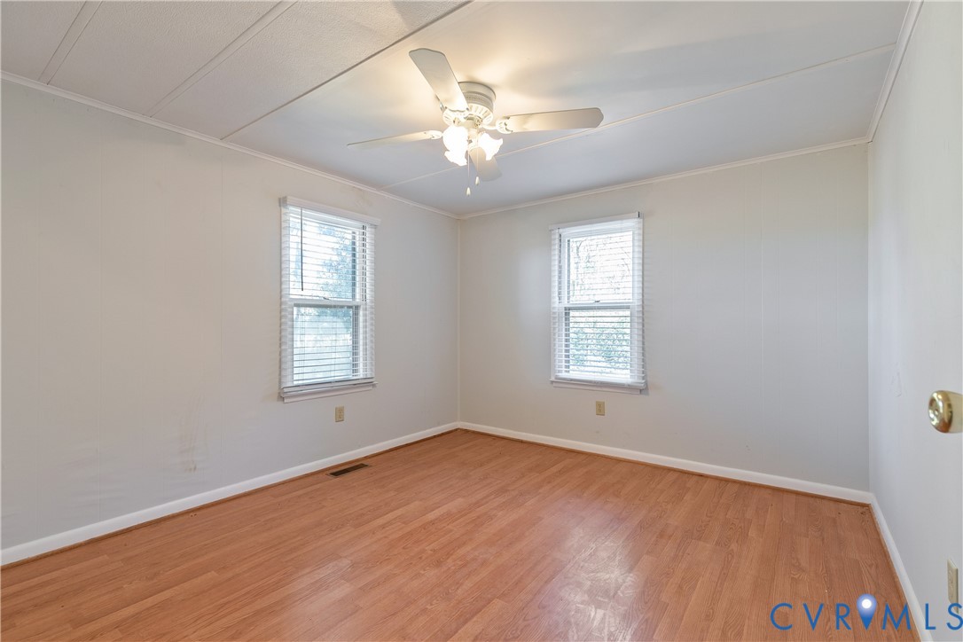 Room featuring wood-finish flooring, dual windows with blinds, and a central ceiling fan with integrated lighting