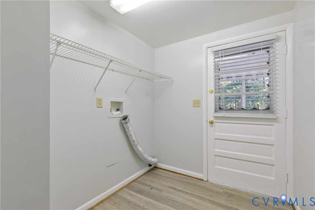 Utility area featuring wood-finish flooring, white wall-mounted shelving, and an exterior door with an integrated window
