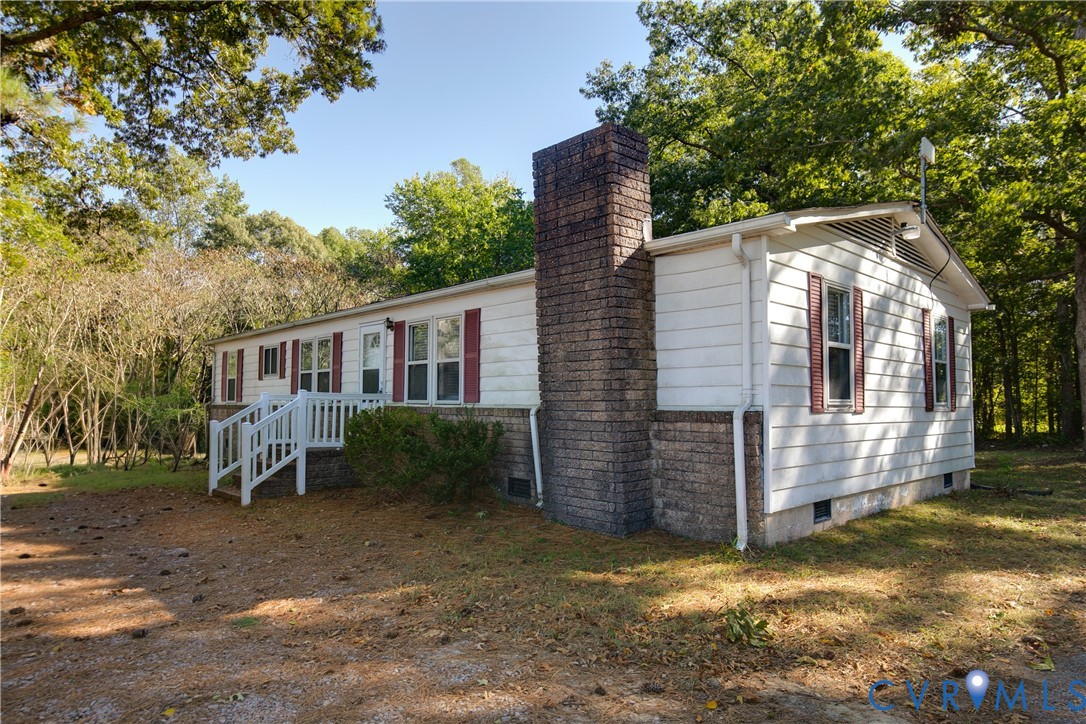 Exterior featuring white siding, a brick masonry chimney, decorative window shutters, and an elevated wooden entry deck Exterior featuring white siding, a brick masonry chimney, decorative window shutters, and an elevated wooden entry deck