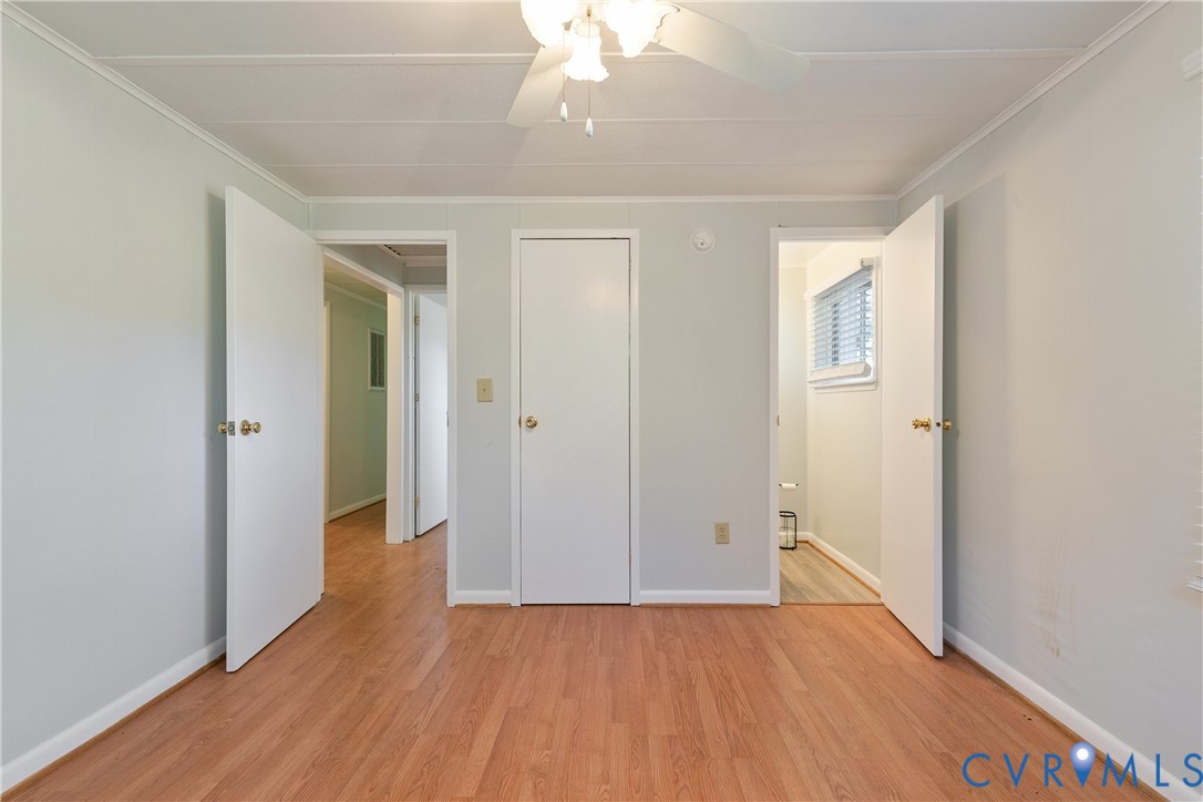 Interior space featuring wood-finish flooring, neutral wall paint, three white interior doors, and a ceiling-mounted fan with light fixture