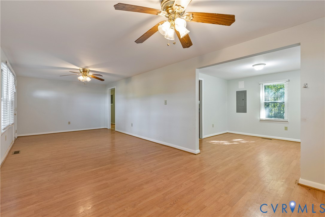 Open interior featuring wood-finish flooring, two ceiling fans with integrated light fixtures, and multi-pane windows Open interior featuring wood-finish flooring, two ceiling fans with integrated light fixtures, and multi-pane windows