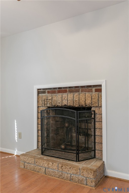 Fireplace featuring a textured stone facade, elevated stone hearth, and white trim molding set against wood-finish flooring Fireplace featuring a textured stone facade, elevated stone hearth, and white trim molding set against wood-finish flooring