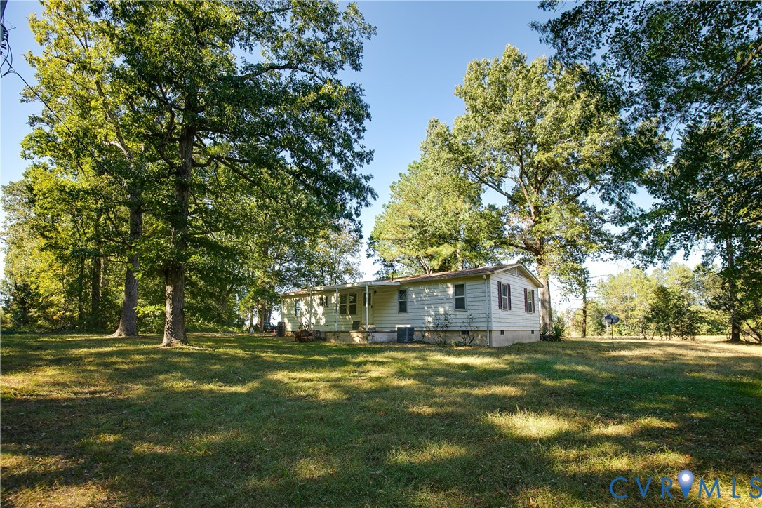 Single-story residence featuring light-colored horizontal siding, a covered front porch, and shutters, situated on a lot with expansive grass and mature trees