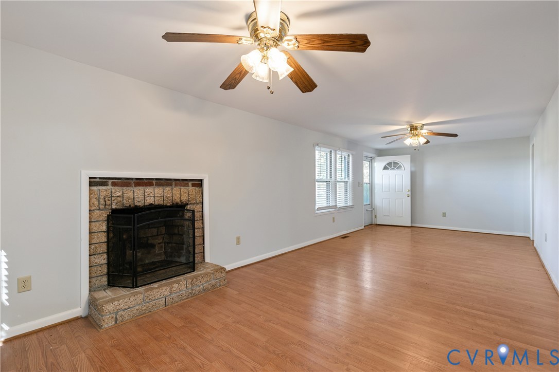 Interior space featuring wood-finish flooring, two ceiling fans with integrated lighting, and a brick fireplace with a raised hearth Interior space featuring wood-finish flooring, two ceiling fans with integrated lighting, and a brick fireplace with a raised hearth