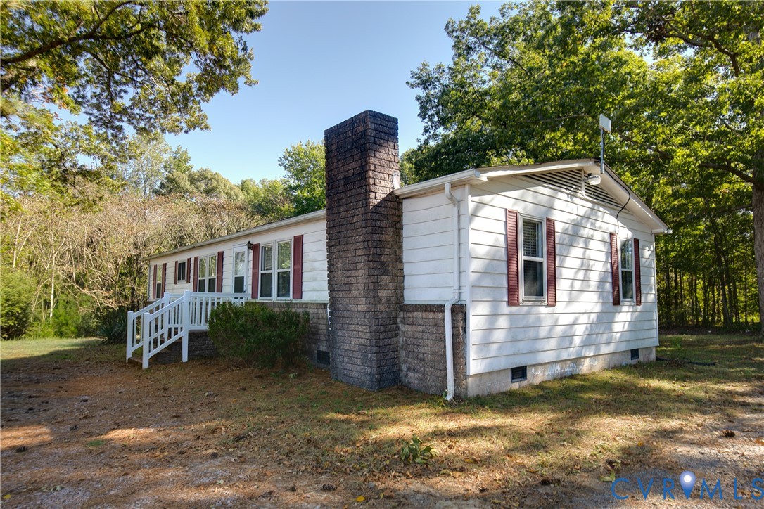 White siding exterior featuring decorative shutters, a prominent brick chimney, and a raised wooden entrance deck
