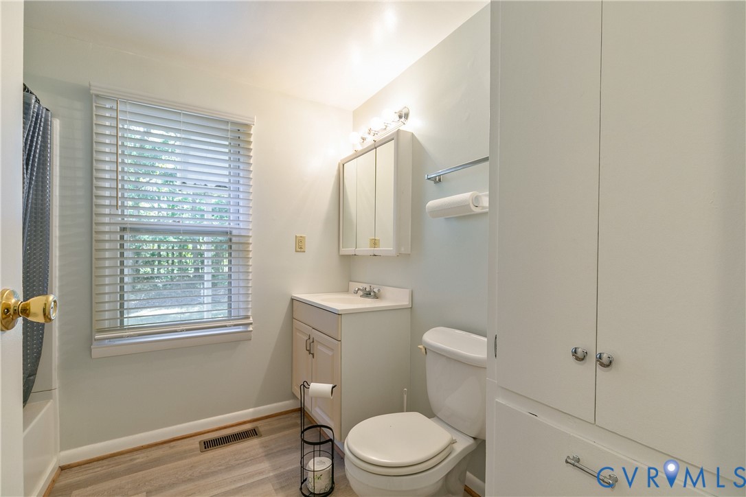 Bathroom featuring wood-finish flooring, a white vanity with integrated sink, a mirrored medicine cabinet, a full-height built-in storage cabinet, and a window with horizontal blinds