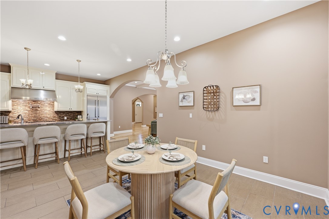 Kitchen featuring white cabinetry, a stone-tiled backsplash, stainless steel appliances, a breakfast bar, and recessed lighting