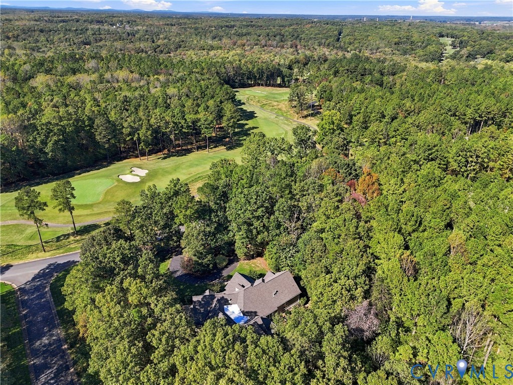 Aerial perspective featuring a multi-gabled roofline, asphalt driveway, dense mature tree canopy, and direct proximity to a golf course fairway