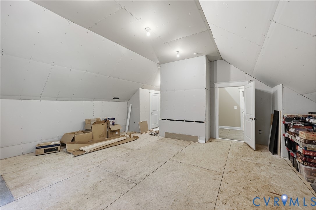 Unfinished space featuring vaulted ceilings, drywall-ready surfaces, plywood subflooring, and two interior doors