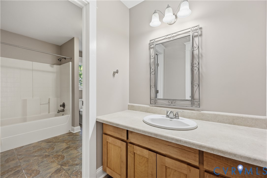 Upstairs Bathroom featuring a wood-finish vanity with a stone-composite countertop, integrated sink, three-light fixture, and tub-shower combination with tiled flooring