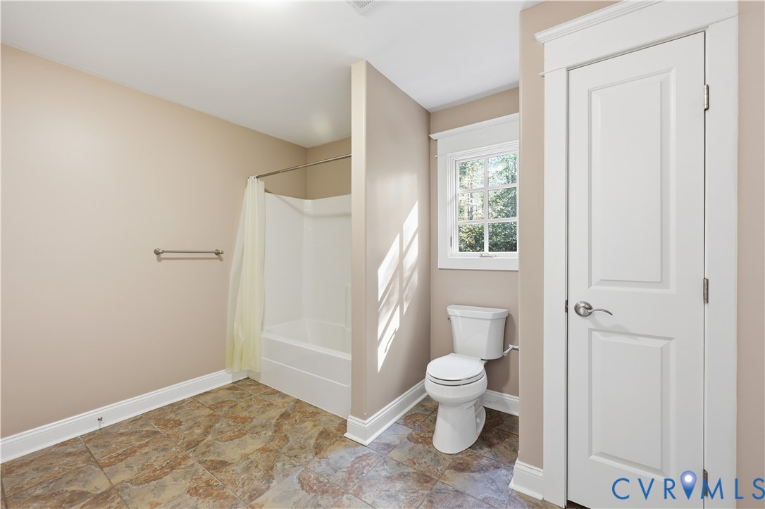 Upstairs Bathroom featuring a white porcelain toilet, a shower-tub combination with a wall-mounted rod, multi-pane window, and patterned stone-finish tile flooring