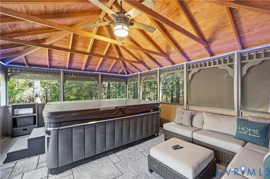 Screened enclosure featuring a wood-plank vaulted ceiling, exposed timber rafters, stone-finish flooring, and a central ceiling fan with integrated lighting